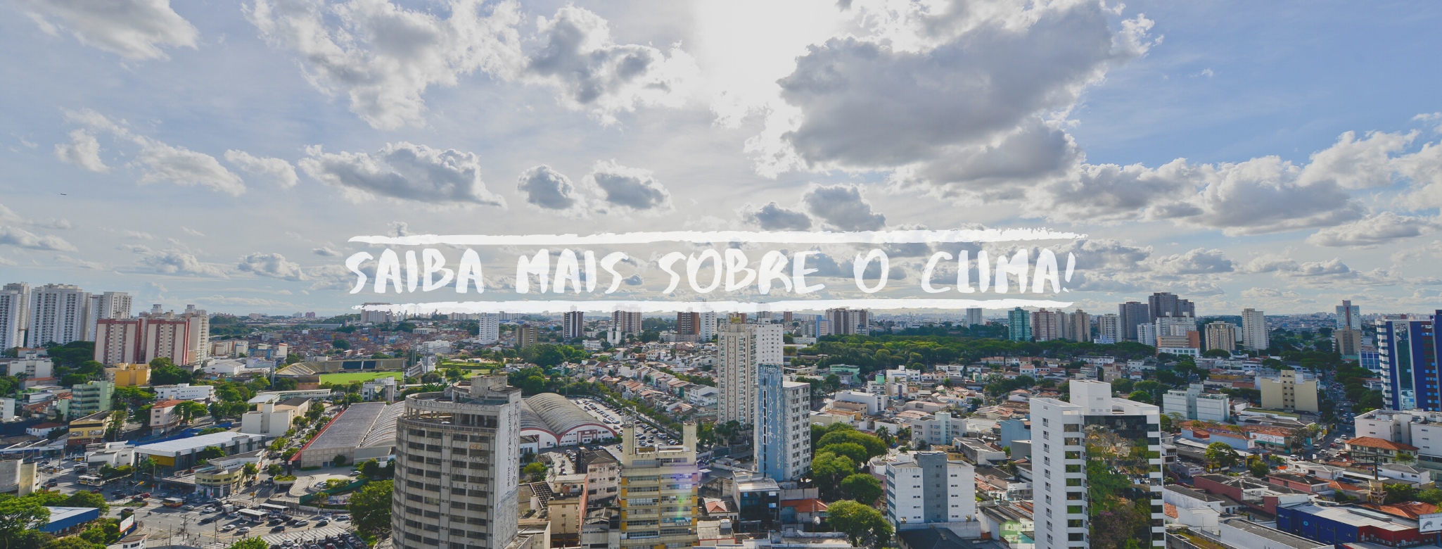 Vista panorâmica de uma cidade sob céu com poucas nuvens. Ao centro, a frase em branco "SAIBA MAIS SOBRE O CLIMA!" sobre uma tarja estilizada. Prédios e casas preenchem o horizonte urbano ensolarado.