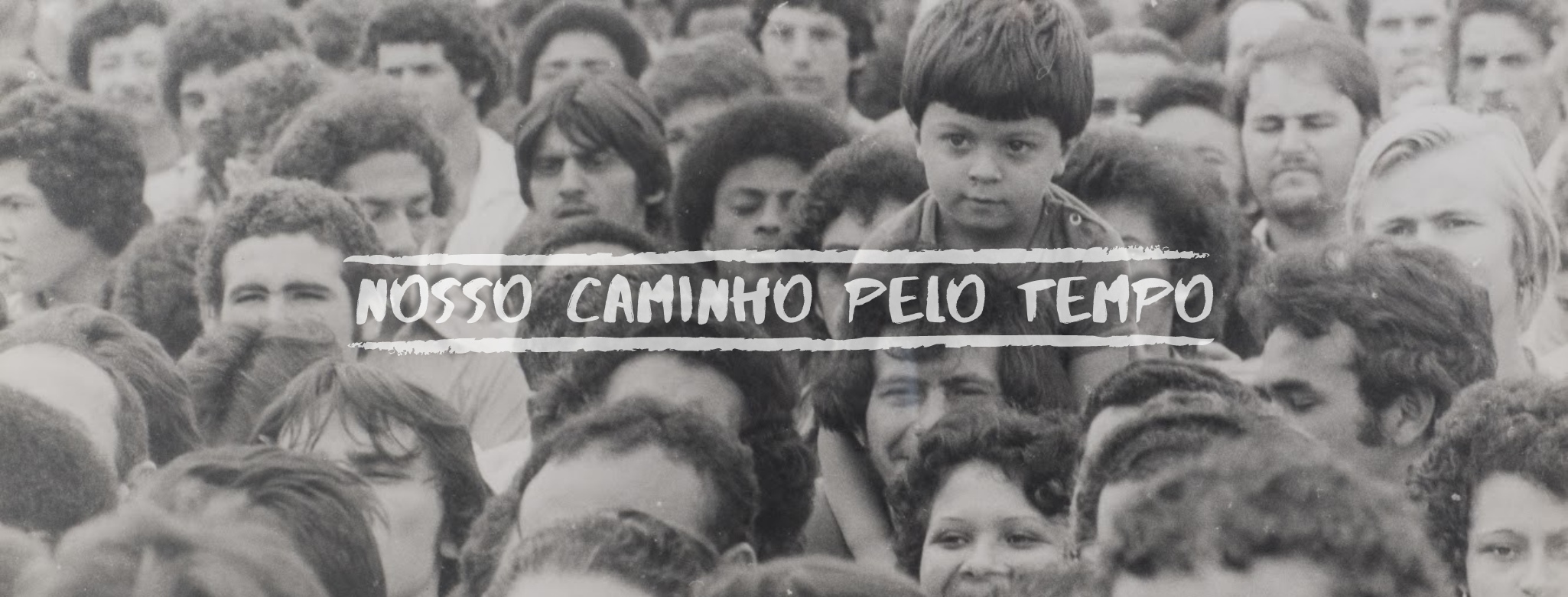 Fotografia em preto e branco de uma multidão densa de pessoas. Ao centro, uma criança se destaca acima das cabeças. Sobre a imagem, a frase "NOSSO CAMINHO PELO TEMPO" em letras brancas estilizadas.